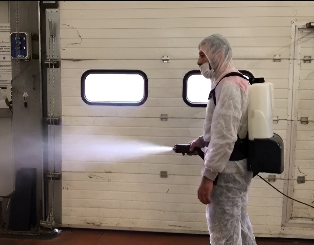 Person in protective gear using a spray machine for sanitizing indoors.